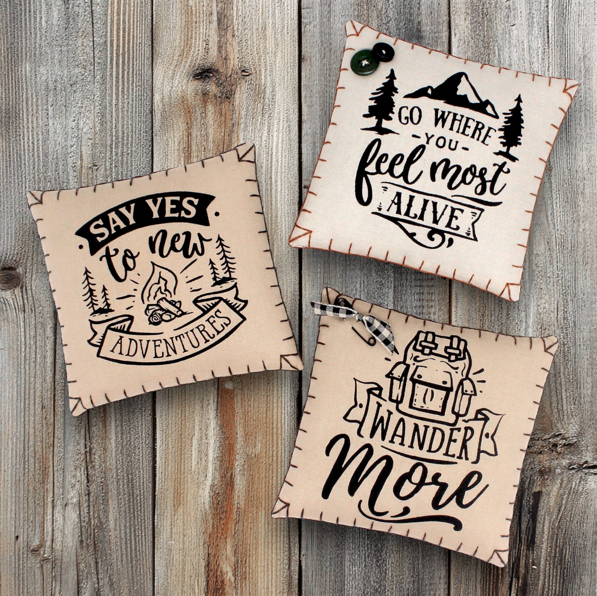 Three motivational pillows with scenic designs and text on a wooden background