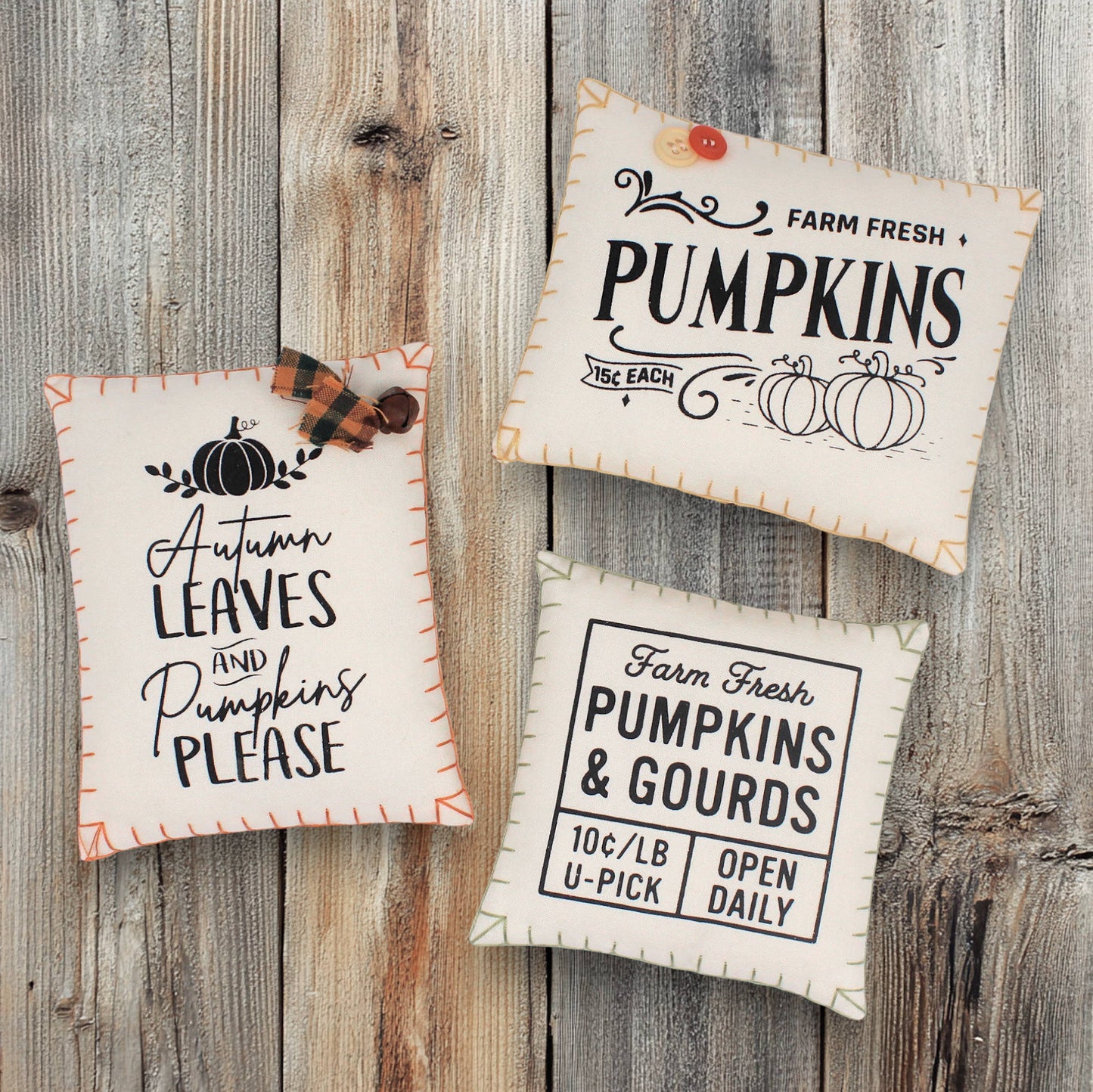 Three decorative mini pillows bowl fillers with autumn-themed text on a wooden surface with leaves.