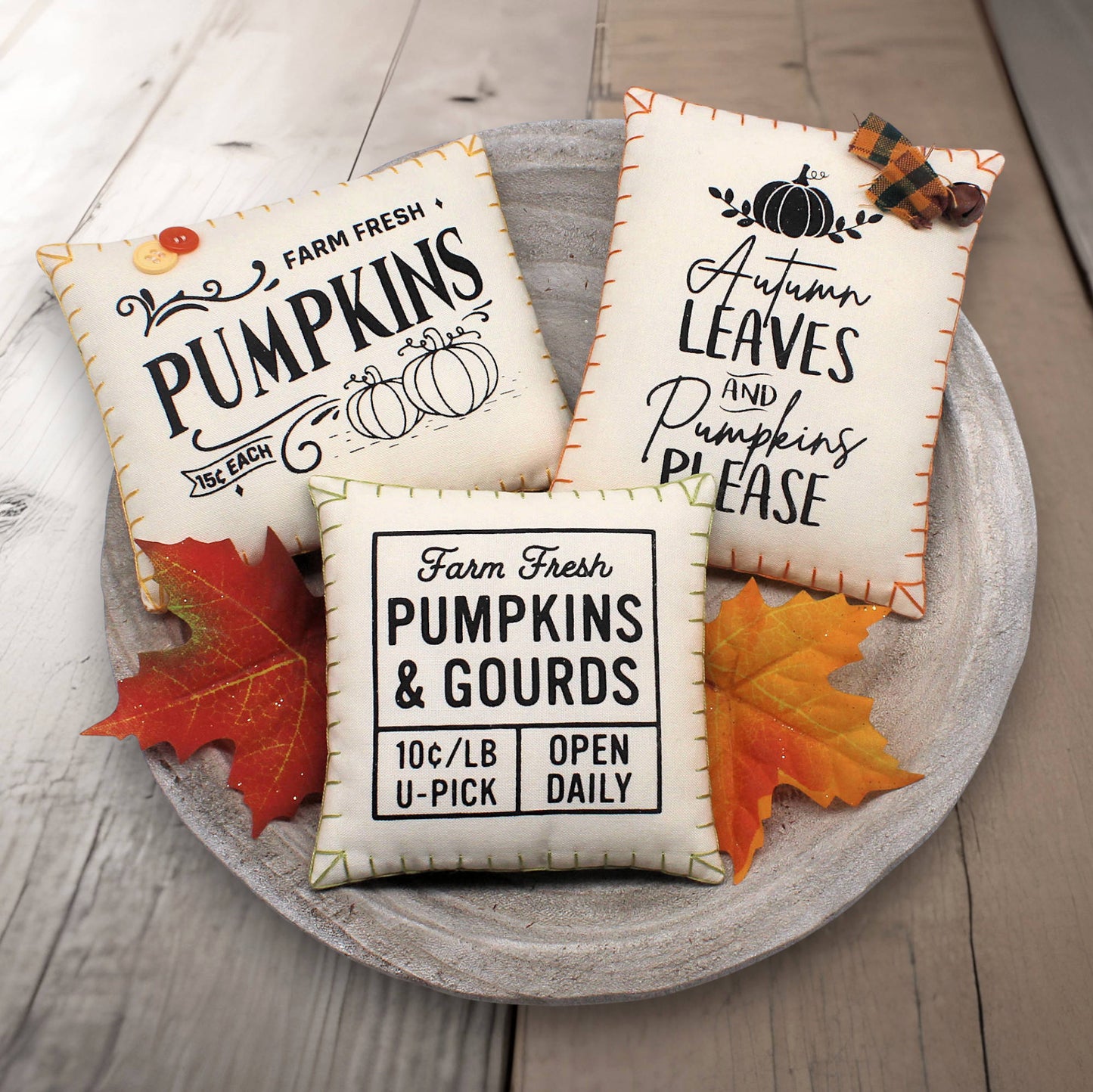 Three decorative mini pillows bowl fillers with autumn-themed text on a wooden surface with leaves.