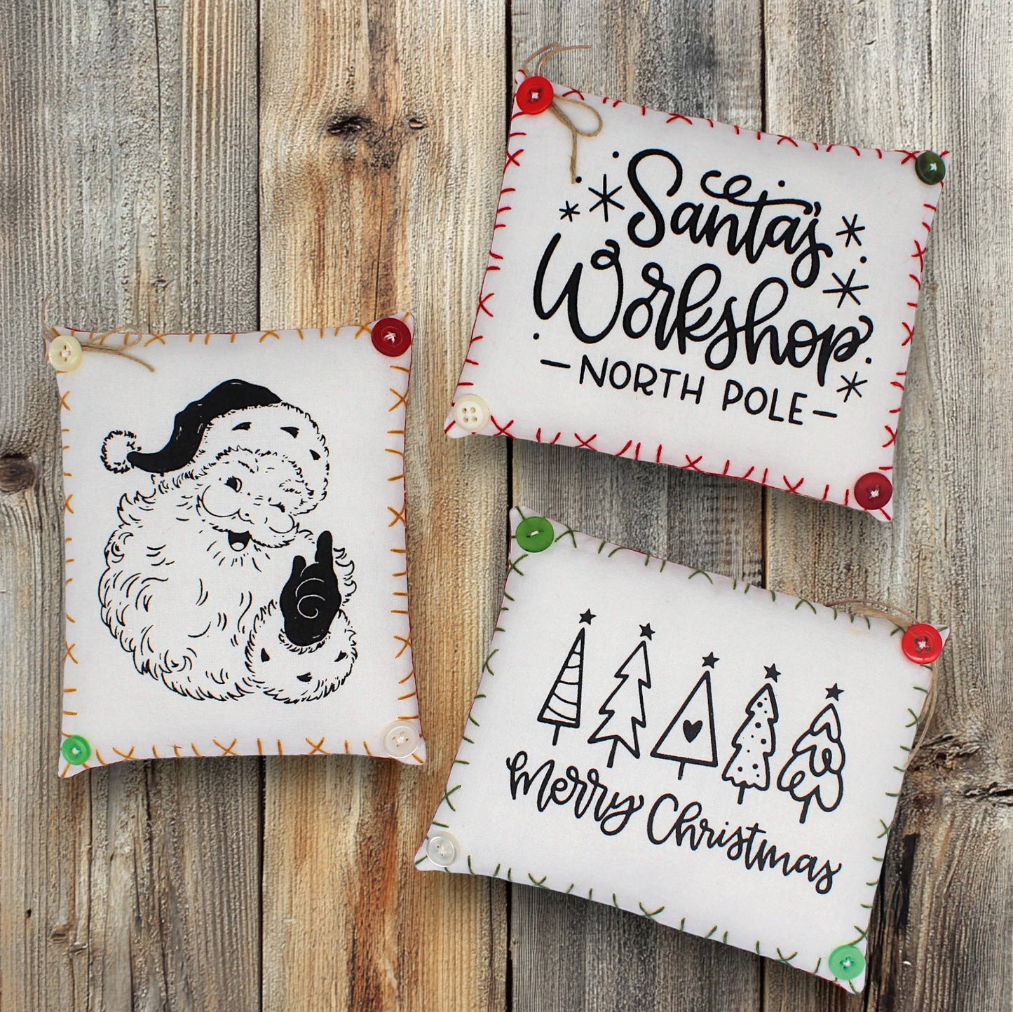 Three Christmas-themed mini pillows on a wooden surface with 'Santa's Workshop North Pole' and 'Merry Christmas' text.