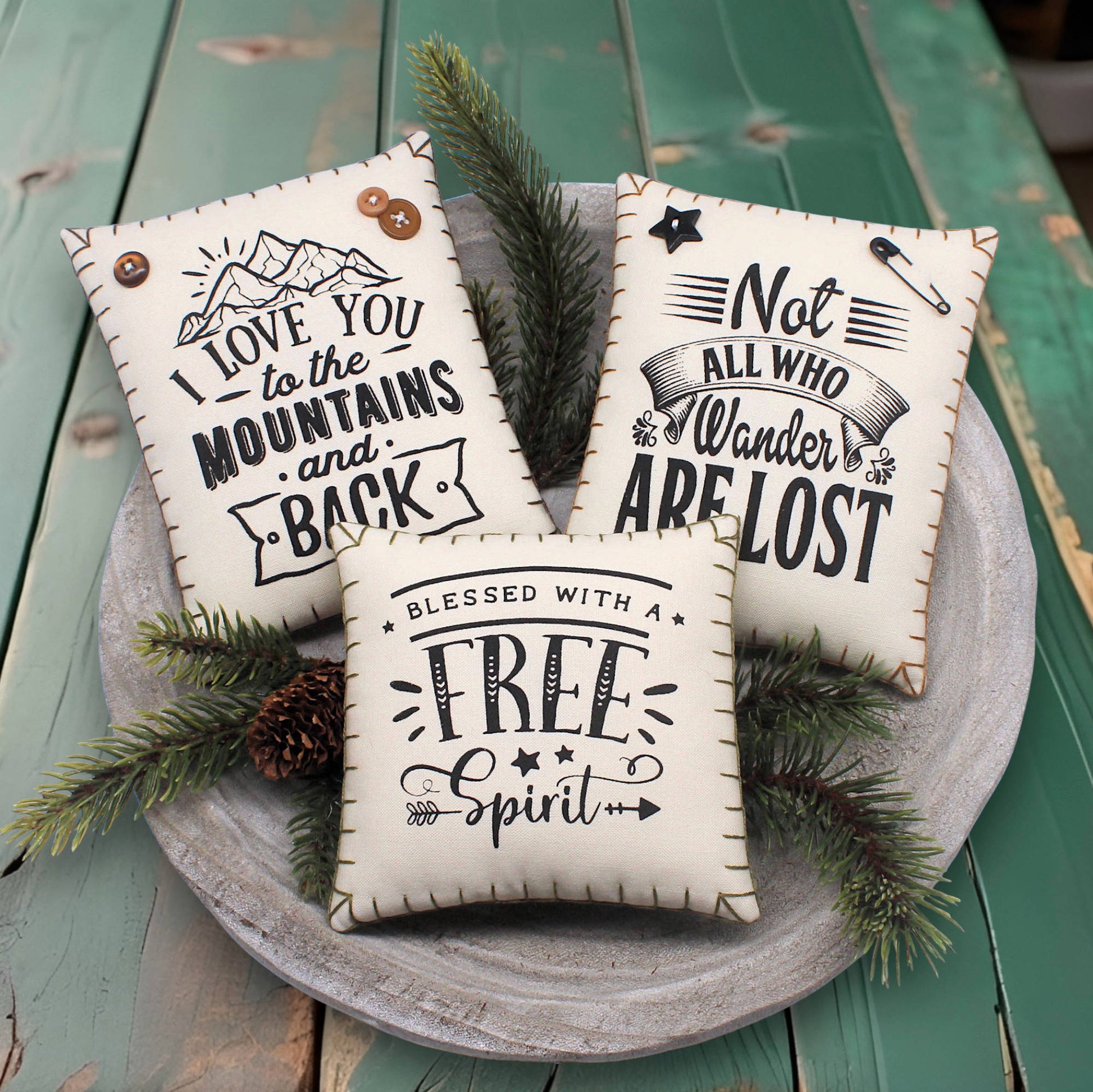Three decorative mini pillow bowl fillers screen-printed with motivational quotes about being in the mountains and having a wandering free spirit