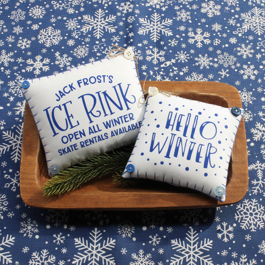 Two decorative pillows with winter-themed text on a wooden tray.