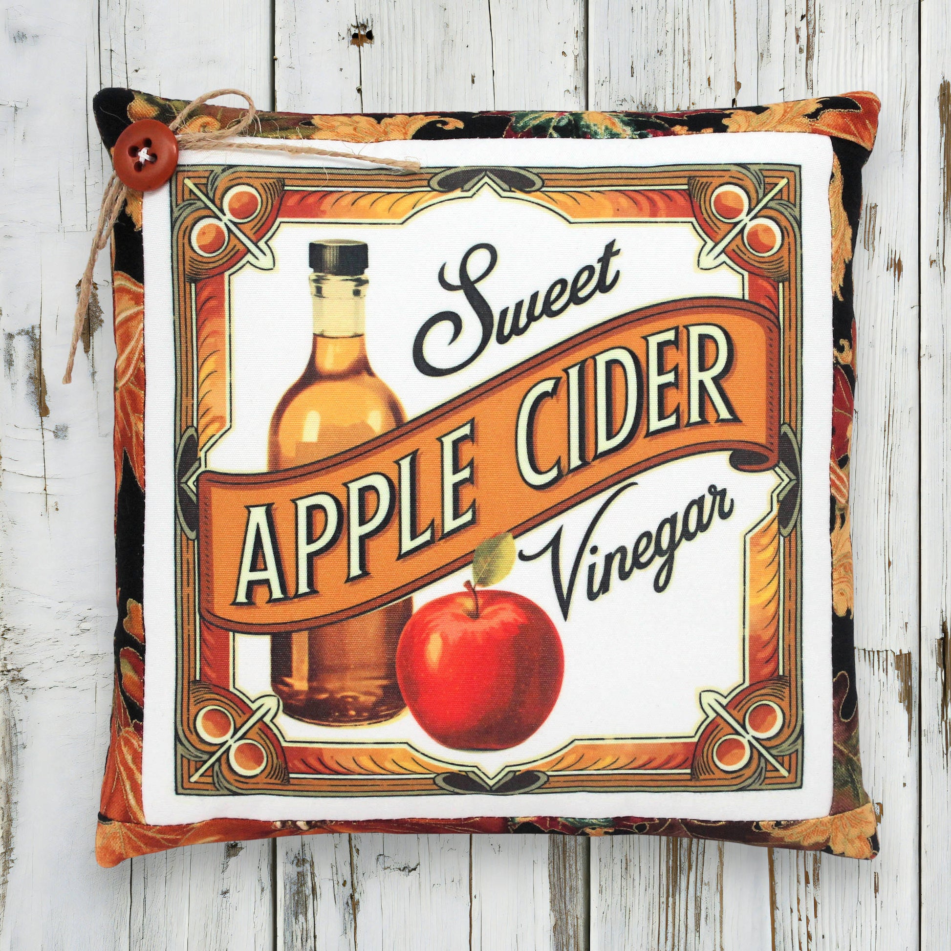 Decorative pillow with a vintage-style 'Sweet Apple Cider Vinegar' design on a wooden background.
