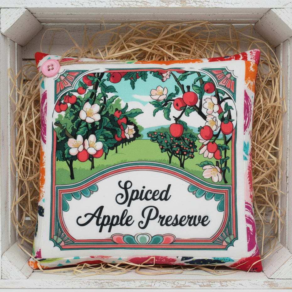 Decorative small pillow for 'Spiced Apple Preserve' with apple tree illustration on a wooden surface.