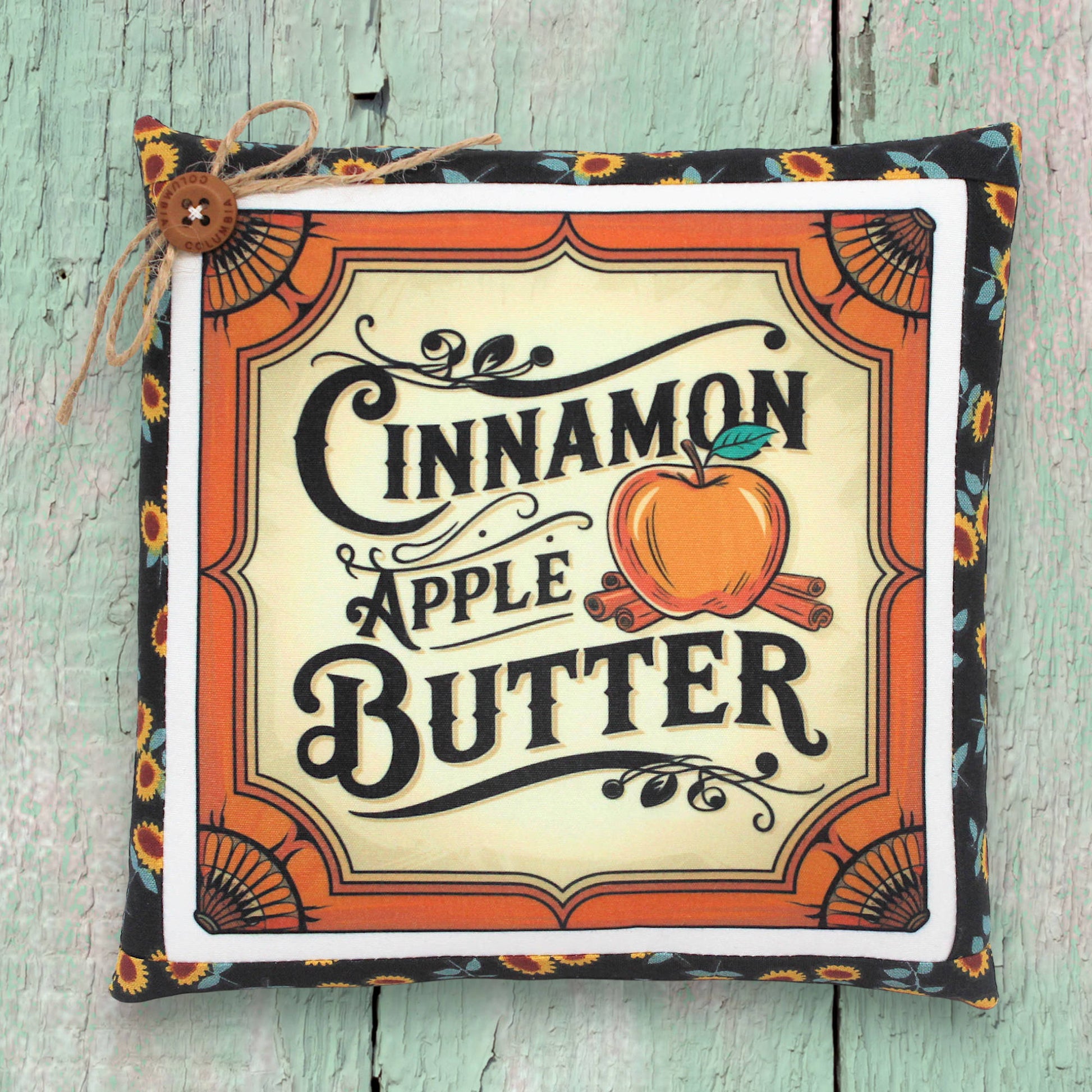 Decorative pillow with 'Cinnamon Apple Butter' text and design on a wooden surface