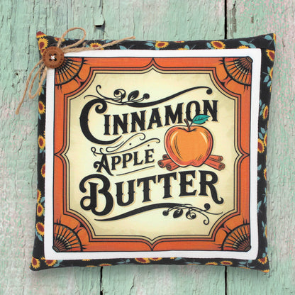 Decorative pillow with 'Cinnamon Apple Butter' text and design on a wooden surface