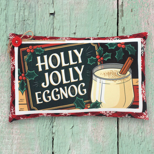Decorative pillow with 'Holly Jolly Eggnog' design on a wooden surface