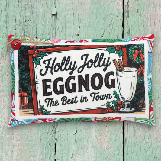 Decorative pillow with 'Holly Jolly Eggnog' text and a glass of eggnog on a wooden surface.