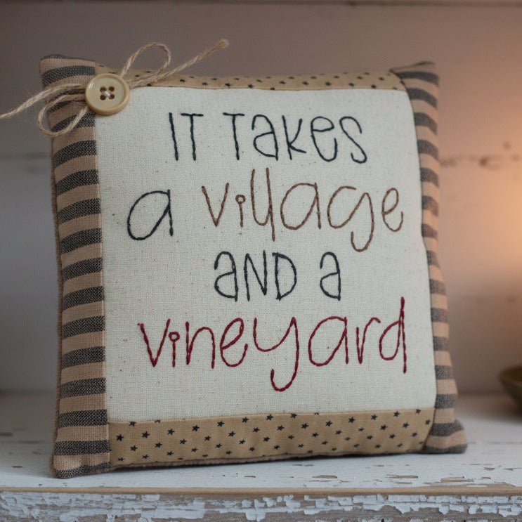 Decorative pillow with text 'It takes a village and a vineyard' on a white background
