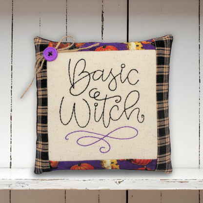 Decorative pillow with 'Basic Witch' text on a wooden shelf