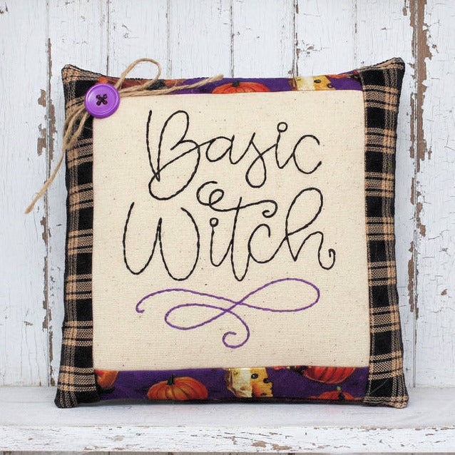 Decorative pillow with 'Basic Witch' text on a wooden shelf